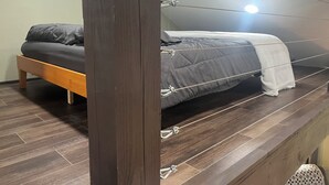 Een slaapkamer met een bed, houten vloer en een plafondlamp.