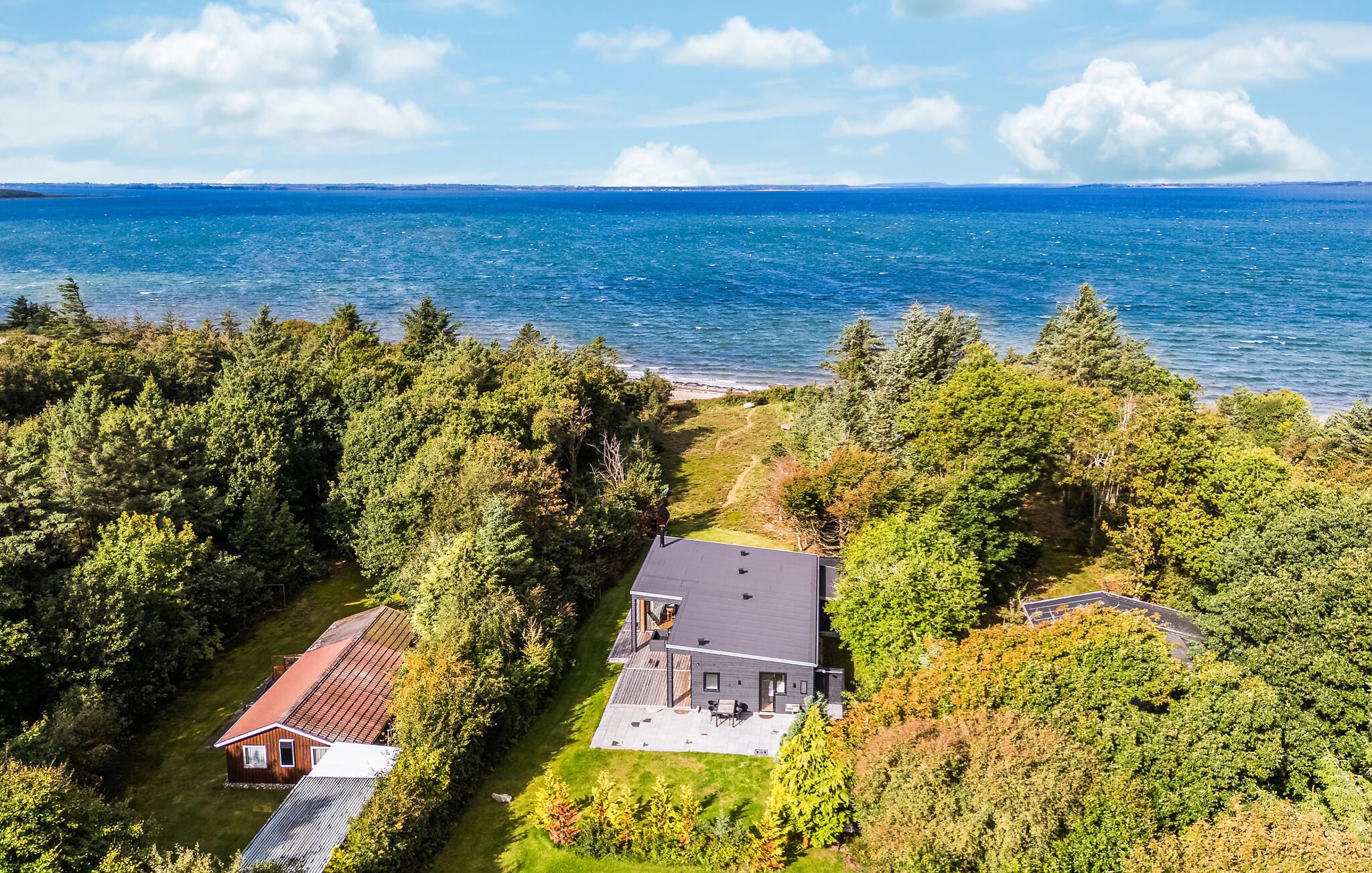 A coastal property with a large house, a smaller cabin, and a beach view.