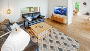 A modern living room with a leather sofa, a wooden coffee table, a TV, and a dining area with chairs. - Cozy home in Spøttrup with sauna (Spøttrup)