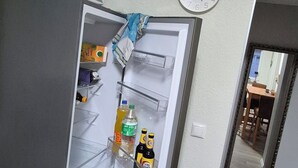 Una cocina con un refrigerador abierto que contiene bebidas y una tetera. Se observa un reloj en la pared.