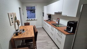 Una cocina compacta con una mesa y sillas de madera, armarios blancos y una cafetera.