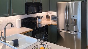 A modern kitchen with green cabinets, stainless steel appliances, a sink, and a fruit basket. - Timberline Retreat - Sleeps 9, large backyard, well stocked kitchen! (Windsor)
