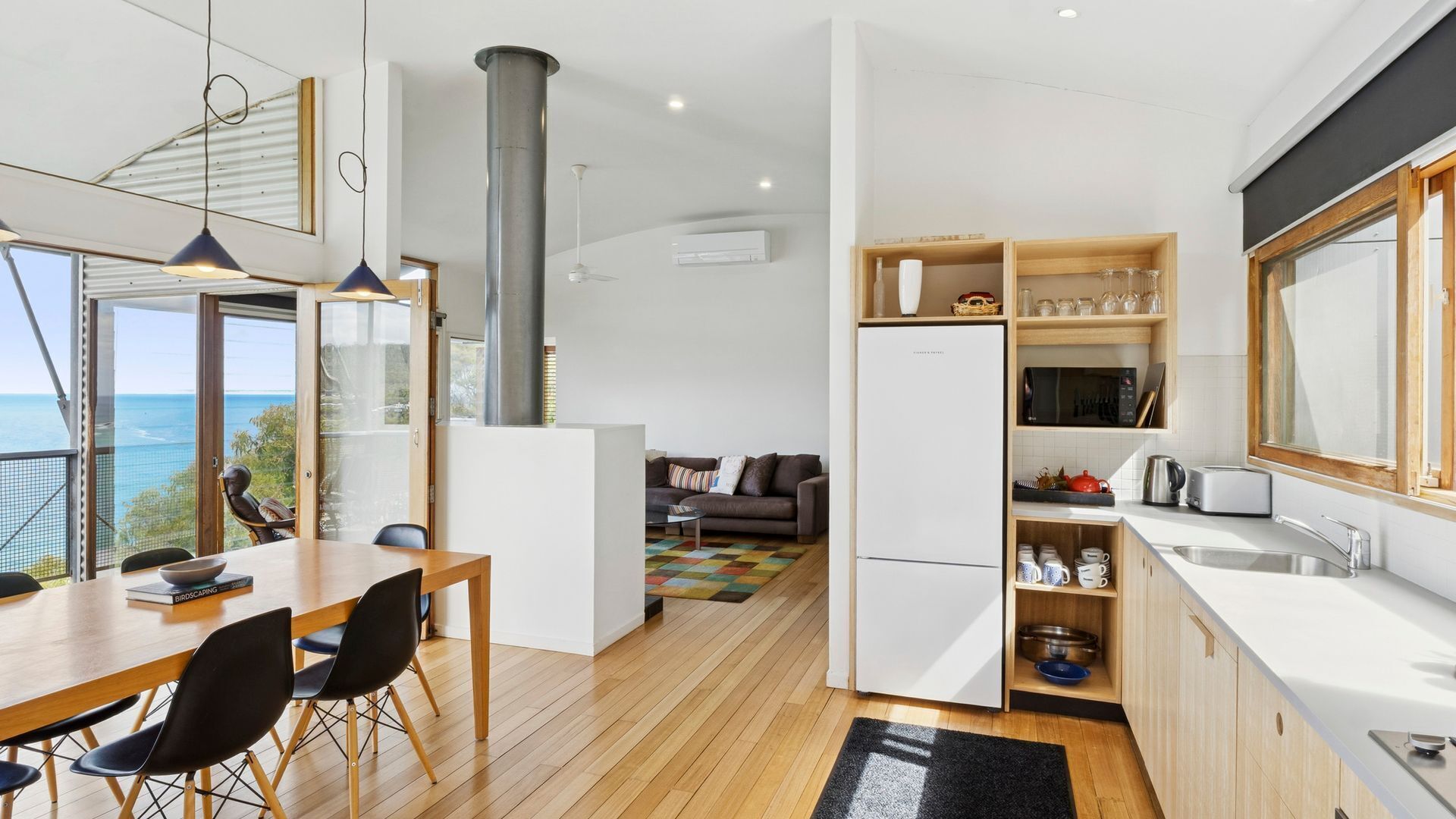 Une cuisine moderne avec vue sur la mer, un coin repas avec une table et des chaises en bois, et un espace de vie chaleureux avec un canapé et une table basse.