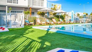 Zona de piscina con césped artificial, sillones reclinables y sombrillas.