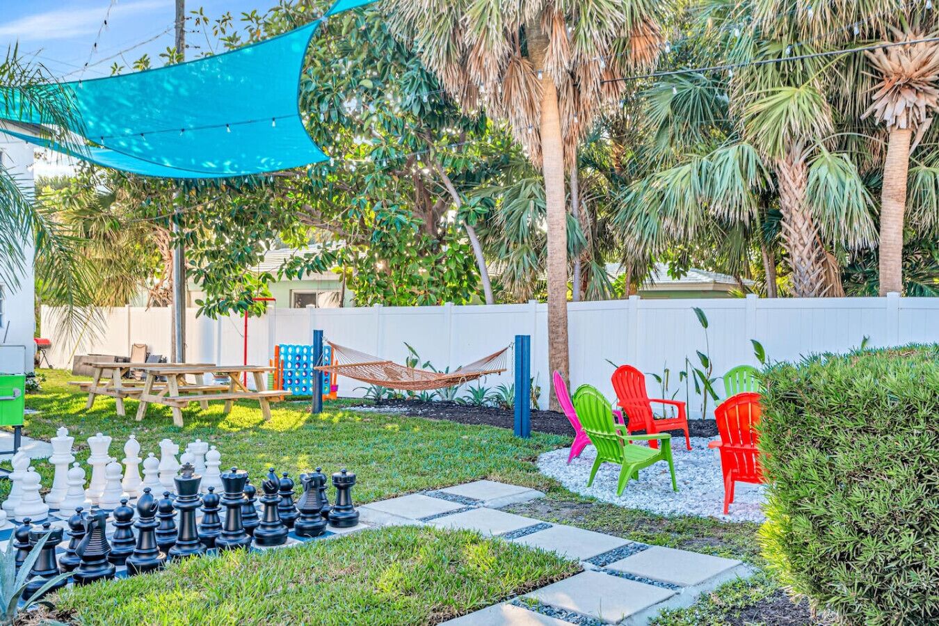 A backyard with a chessboard, picnic table, hammock, and colorful chairs.