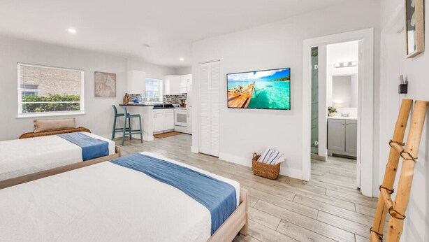 Una habitación de hotel moderna con dos camas, un kitchenette, un televisor y vistas al mar.