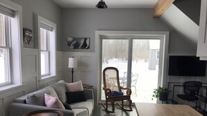 Un salon avec un canapé gris, un fauteuil à bascule en bois, une petite table et un téléviseur fixé au mur.
