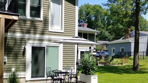Une maison à deux étages dotée d’un patio comprenant une table et des chaises, un espace extérieur couvert aménagé en coin salon, et une pelouse bien entretenue.