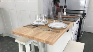 Une cuisine dotée d’un îlot central en bois, aménagé pour servir de table à manger, et équipé de verres et de couverts.