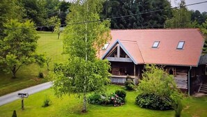 Une maison avec un toit en pente, une véranda et une pelouse bien entretenue, agrémentée de diverses plantes et fleurs.