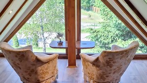 Une pièce avec deux fauteuils placés face à une petite table et donnant sur un jardin grâce à une grande fenêtre.