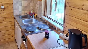 Une cuisine de taille réduite, équipée d’une cuisinière, de deux éviers et d’une fenêtre donnant sur un paysage verdoyant.
