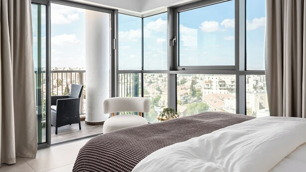 A modern hotel room with a large bed, a chair, and a balcony with a city view. - MR Savyon view 2BR with 2 balcony 77 (Jerusalem)