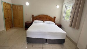 Un dormitorio con una cama de madera, dos mesitas de noche, una ventana con cortinas y una puerta.