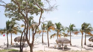 A beach with palm trees, thatched umbrellas, and lounge chairs. - Seashell Sanctuary -S2-107- 2 bed, 2 bath (Punta Chame)