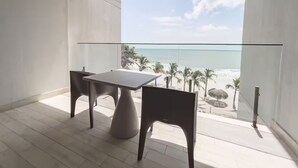 Ein Balkon mit Tisch und Stühlen, der Blick auf einen Strand mit Palmen und dem Meer freigibt.