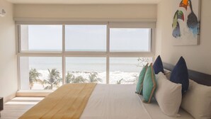 Ein Schlafzimmer mit einem großen Fenster, einem Bett mit gelber Tagesdecke und einem Vogelgemälde an der Wand.