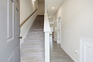 A hallway with a carpeted staircase, white walls, and a wooden floor.