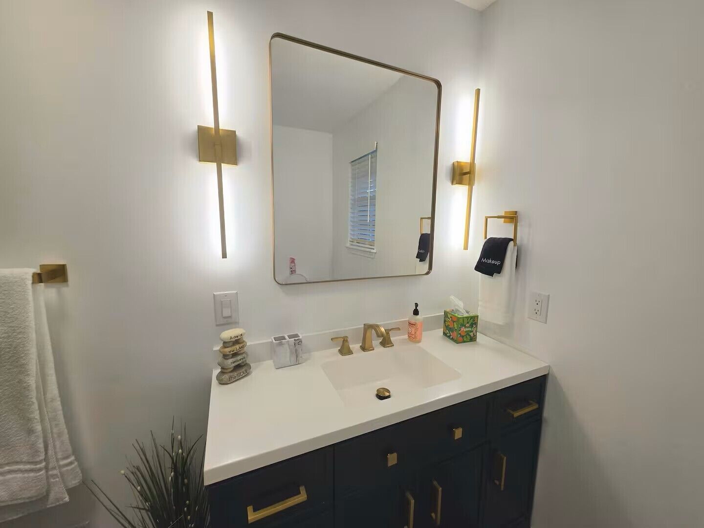 A modern bathroom with a white vanity, gold fixtures, and a large mirror.