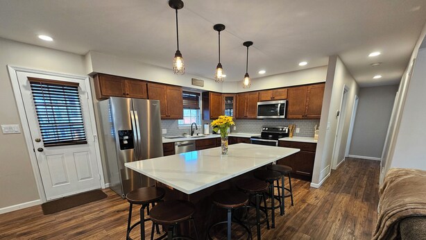 Una cocina moderna con armarios de madera, electrodomésticos de acero inoxidable y una isla central con taburetes de bar.