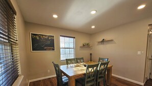 Un comedor con una mesa y sillas de madera, una ventana con persianas, un mapa en la pared y una guitarra.