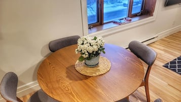 A round wooden table with a woven placemat, surrounded by four grey upholstered chairs.