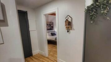 A hallway with a wooden floor leading to a bedroom with a bed and a wall-mounted decoration.