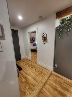 Un pasillo con piso de madera que conduce a un dormitorio con cama y un adorno en la pared.