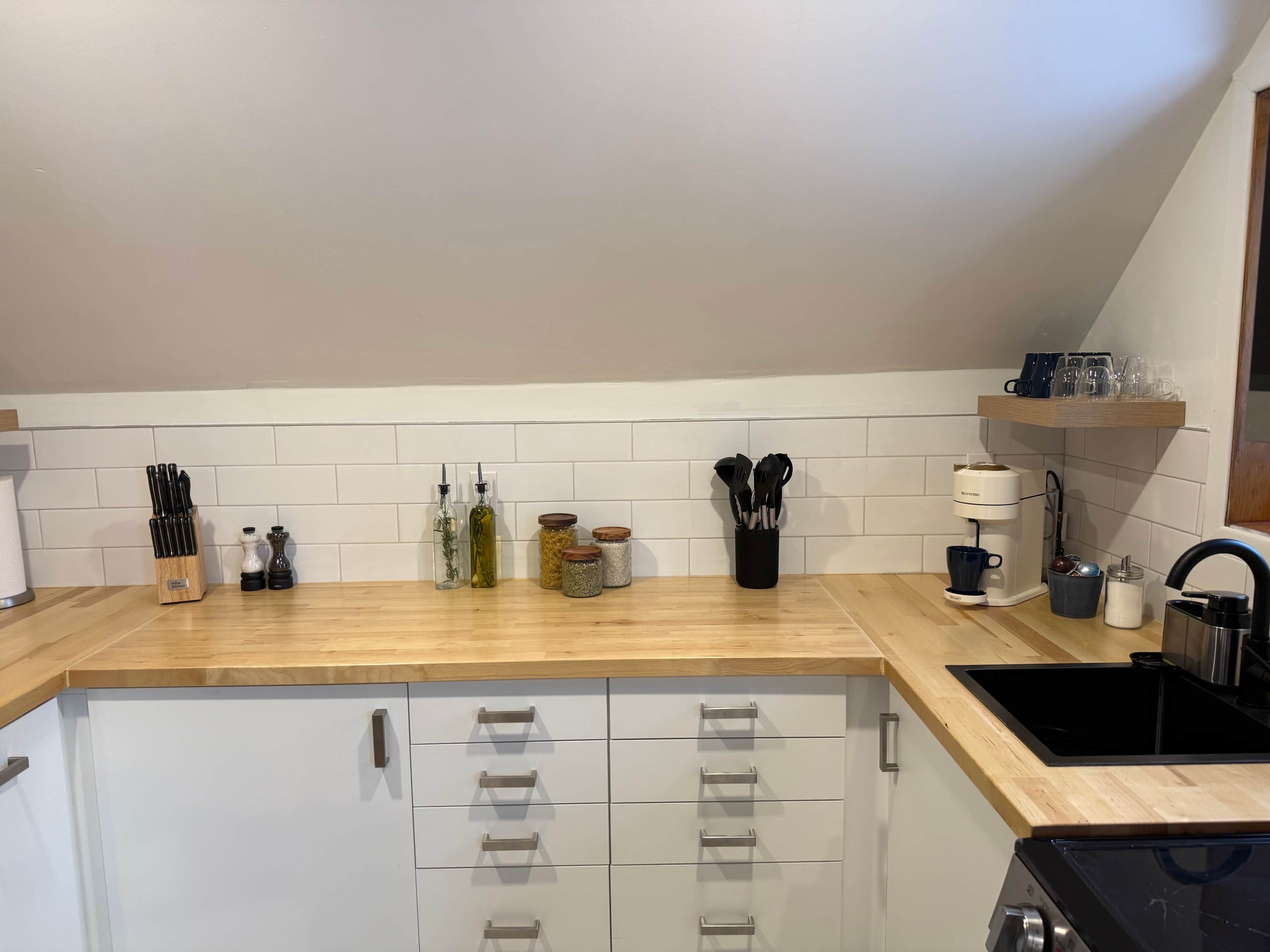 A kitchen with a wooden countertop, white cabinets, and a black stove.