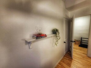 Un pasillo con un estante blanco que contiene libros y una planta, que conduce a una habitación con una puerta.