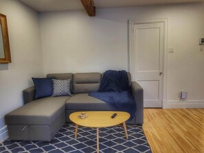 Un salon avec un canapé d’angle gris, une petite table basse ronde et un tapis à motifs.
