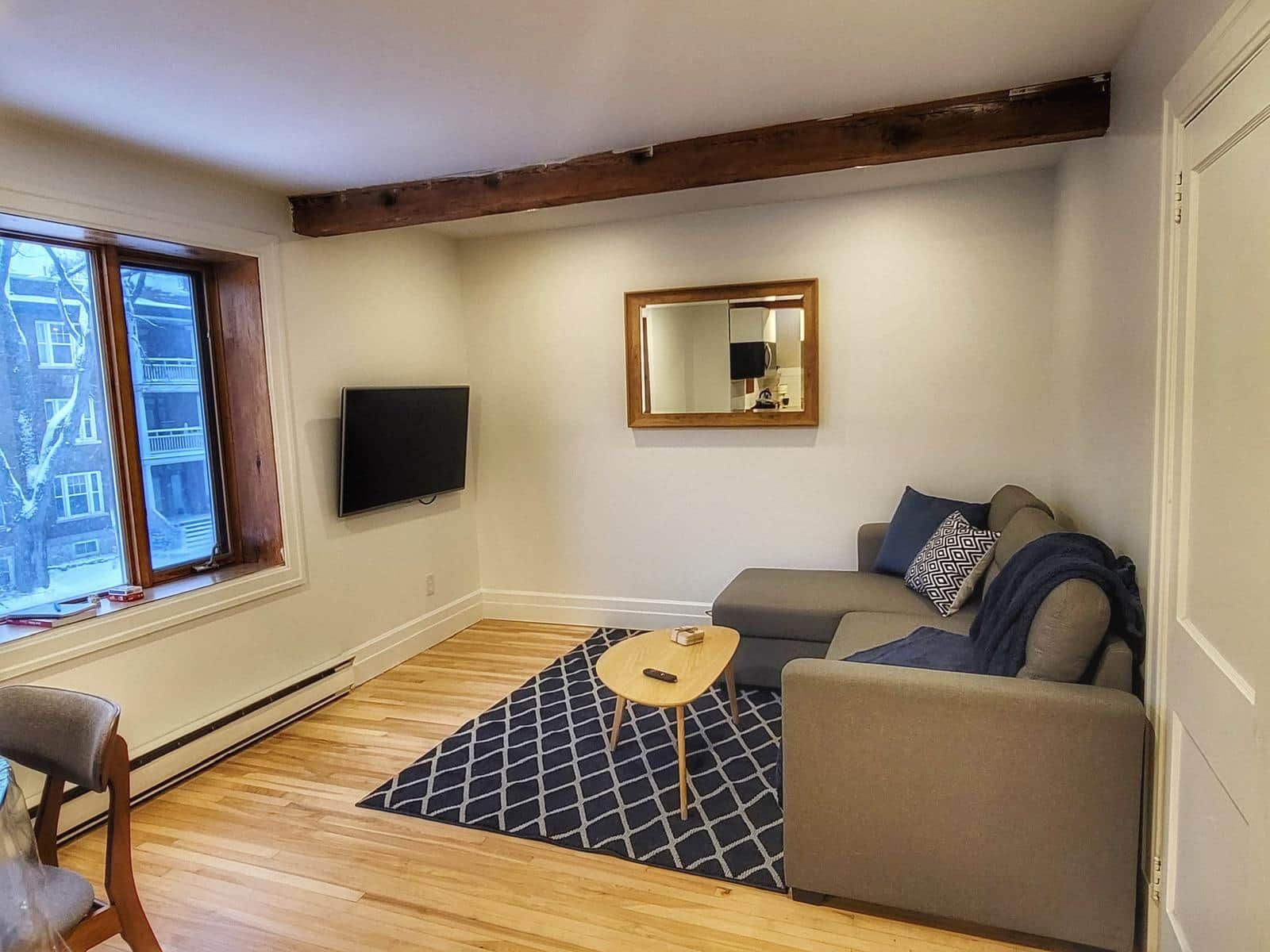 Una sala de estar con un sofá, una mesa de centro, un televisor, un ventanal y un espejo.