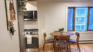 A modern kitchen with a microwave, oven, and sink, a wooden dining table with chairs, and a large window with a view of buildings. - Brilliant 1-bedroom apartment with AC in charming Québec (Québec)