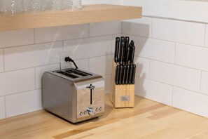 Een keuken met een broodrooster, een messenblok en een witte betegelde spatwand.