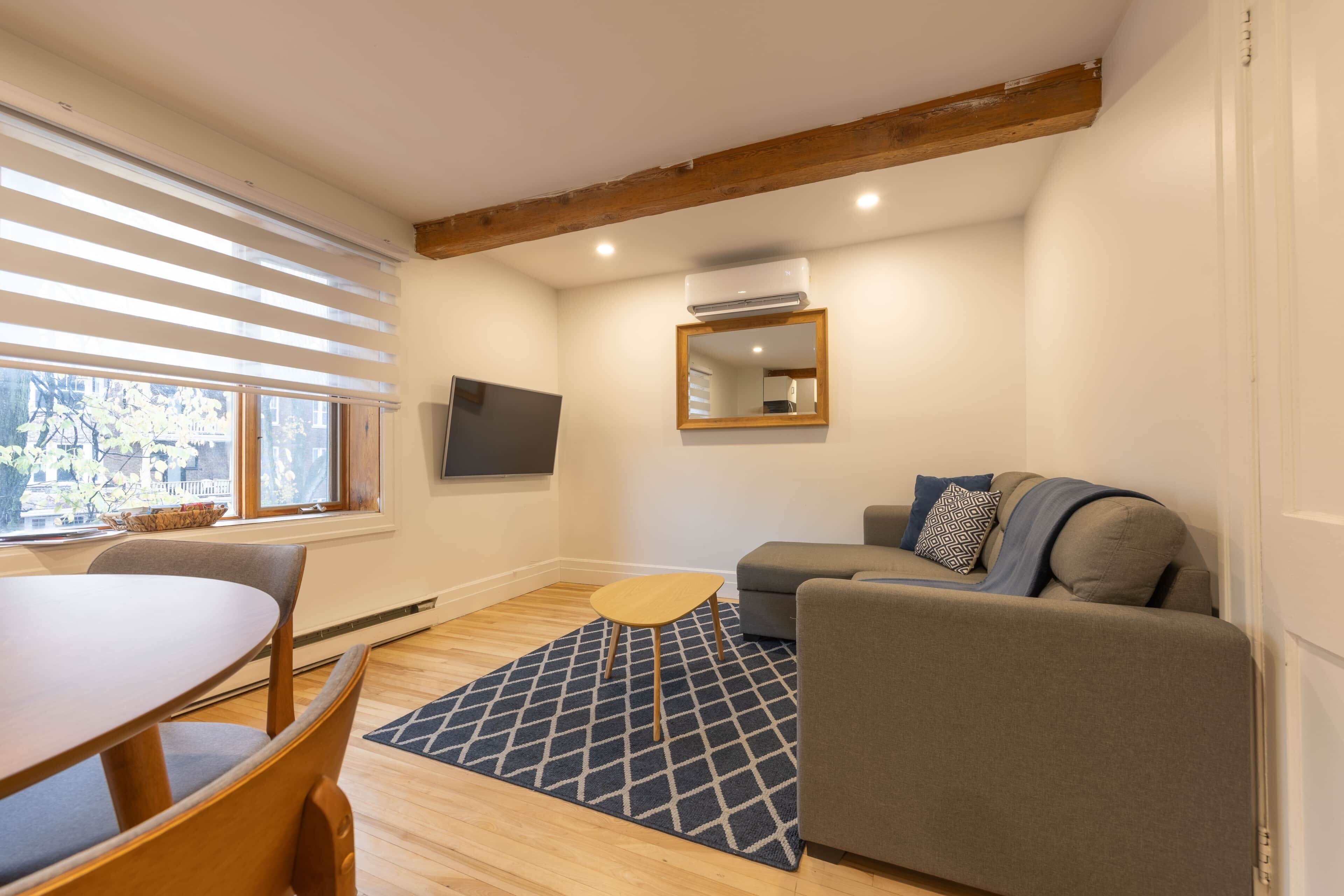Olohuoneessa on sohva, pieni pöytä, televisio ja ikkuna, jossa on sälekaihtimet.