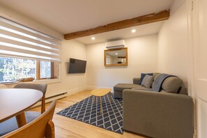 Een woonkamer met een bank, een salontafel, een televisie en een raam met zonwering.