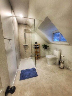 Une salle de bain moderne avec une douche à parois de verre, des toilettes, une petite fenêtre et un tapis bleu.
