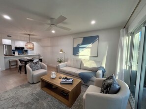 A modern living room with a sofa, coffee table, and a dining area with a kitchen in the background.