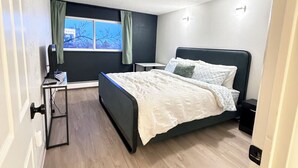 A bedroom with a bed, a desk, a chair, a window with curtains, and a door. - Penthouse condo in central Cheesman Park! (Denver)