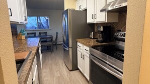 A modern kitchen with white cabinets, stainless steel appliances, and a wooden floor. - Penthouse condo in central Cheesman Park! (Denver)