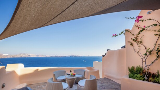 Eine Terrasse mit Korbmöbeln, einem Tisch mit Getränken und Blick aufs Meer.