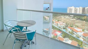 A balcony with a table and chairs, a view of the sea, and a building in the background. - U-GO Torre Areia en Cabo Tortuga (Santa Marta)