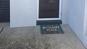 Eine Tür mit einem Metallgitter, eine Fußmatte mit dem Schriftzug „MY HAPPY PLACE“ und ein Betonboden.