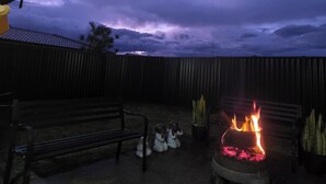 Ein Terrassenbereich im Freien mit Feuerstelle, einer Bank und Lichterketten.
