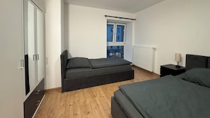 A modern bedroom with a bed, a sofa bed, a nightstand, and a window with blinds. - Central Düsseldorf Apartment: 2 Beds, WiFi, Elevator – Close to Hbf & Fair (Düsseldorf)