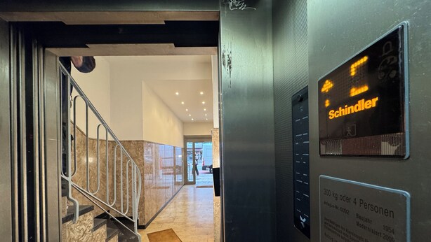 An elevator interior with a digital display, a plaque with historical information, and a staircase leading to a lobby area. - Central Düsseldorf Apartment: 2 Beds, WiFi, Elevator – Close to Hbf & Fair (Düsseldorf)