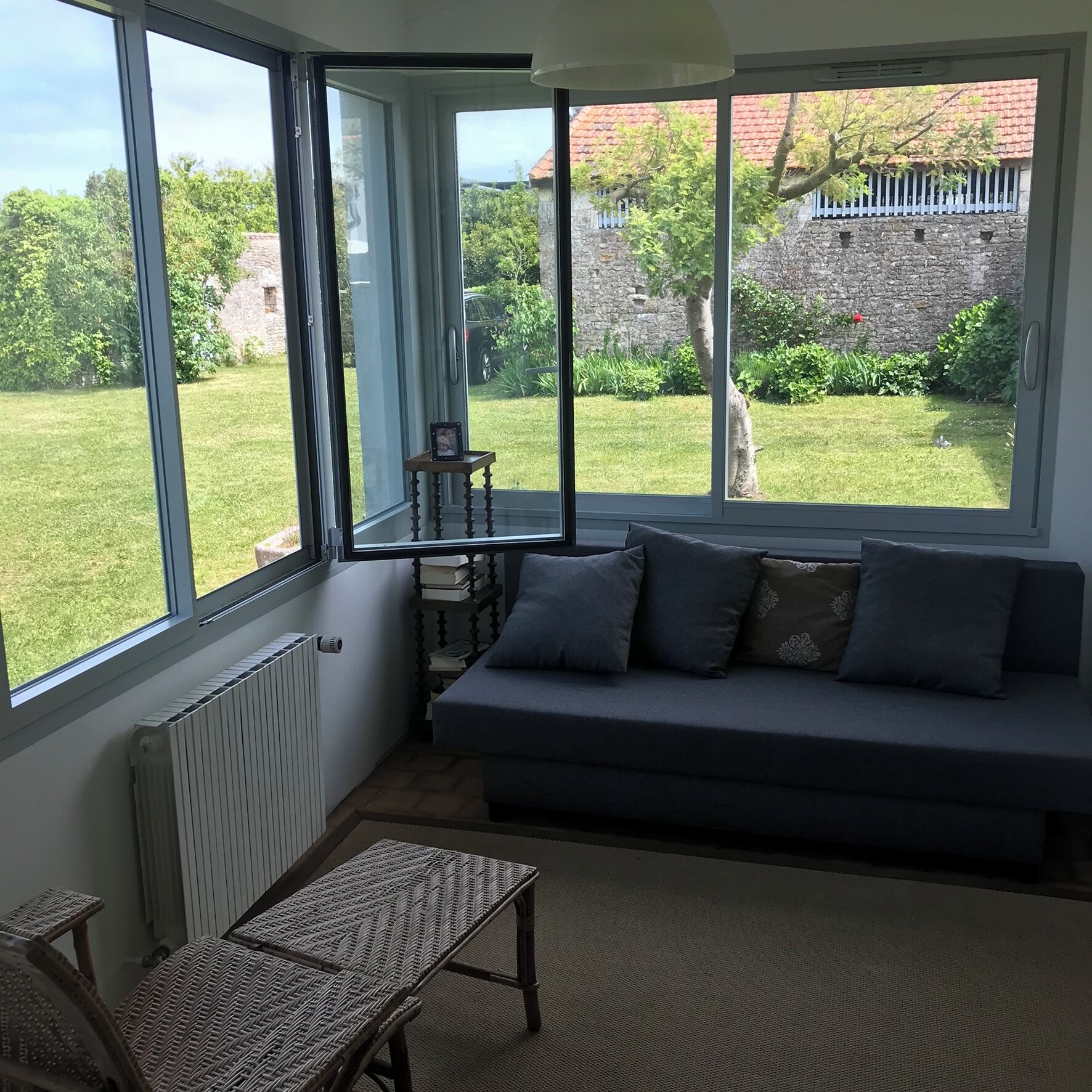 Un salon chaleureux avec un canapé gris, une petite table et une vue sur un jardin grâce à de grandes fenêtres.