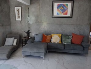 Ein modernes Wohnzimmer mit einem grauen Ecksofa, einem kleinen Beistelltisch und einem gerahmten abstrakten Gemälde an der Wand.