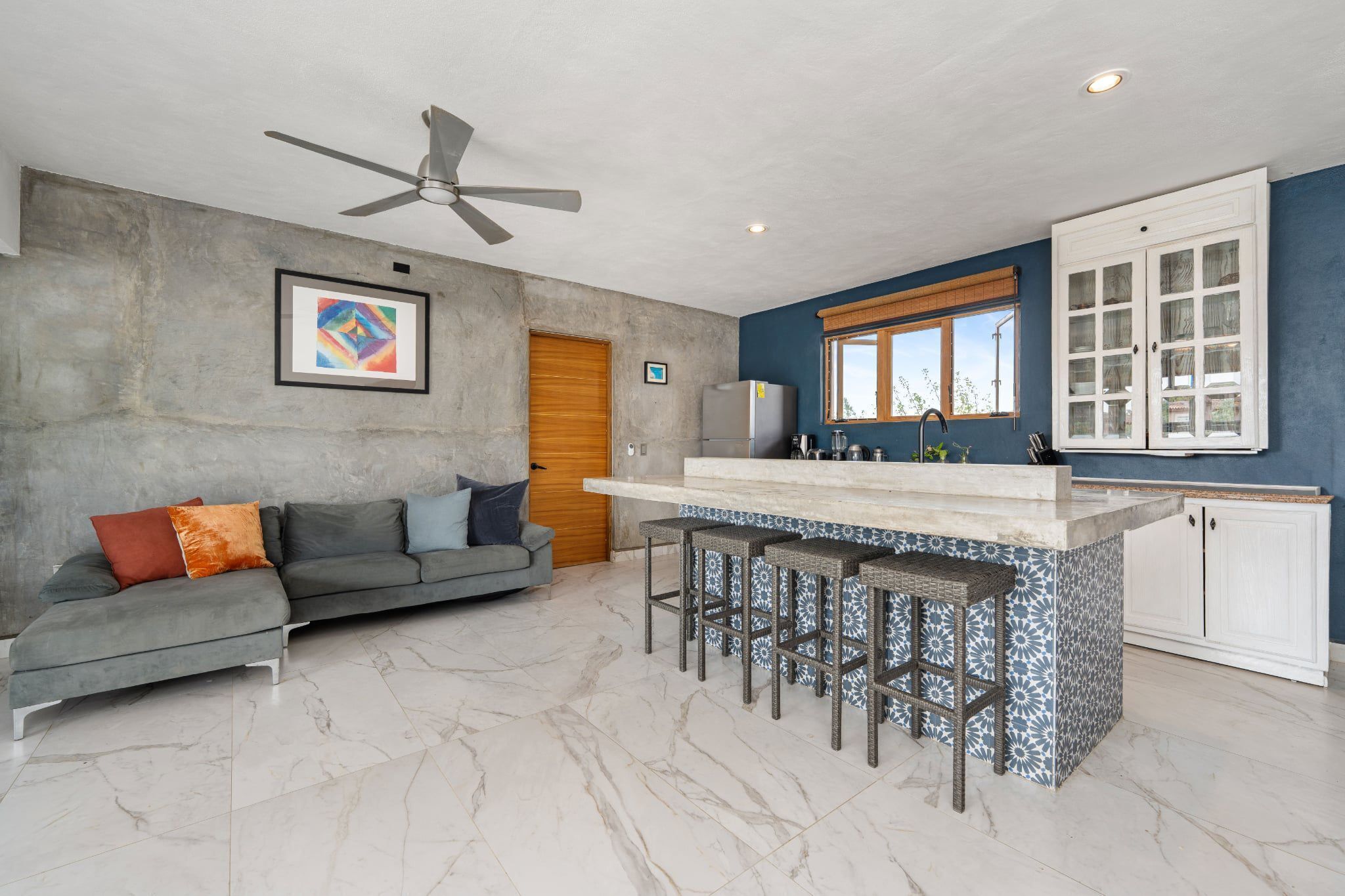 A modern kitchen with a bar area, a ceiling fan, and a dining space with a sofa and cushions.