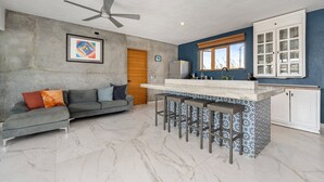 A modern kitchen with a bar area, a ceiling fan, and a dining space with a sofa and cushions. - Amazing Sea & Mountains Views
3 bed 4n half bathroom
Private 7m by 3mChukum pool (San Jose del cabo)